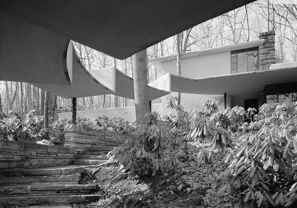 Black and white architectural photograph of cantilevered terraces, stone steps and woodland